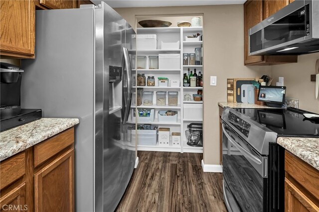 kitchen with dark wood finished floors, brown cabinetry, light stone countertops, and stainless steel appliances