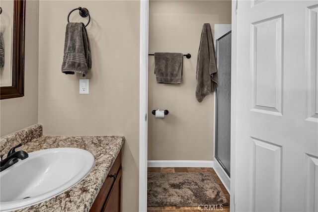 full bath featuring a stall shower, vanity, and baseboards