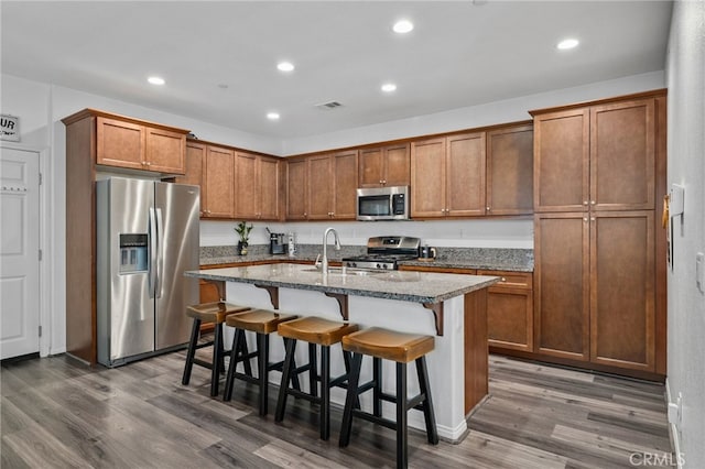 kitchen with dark wood-style floors, visible vents, a sink, stainless steel appliances, and a kitchen bar