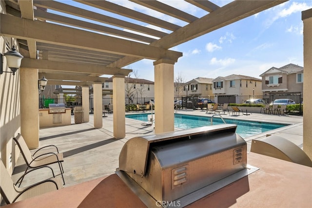 community pool featuring fence, a residential view, exterior kitchen, a grill, and a pergola