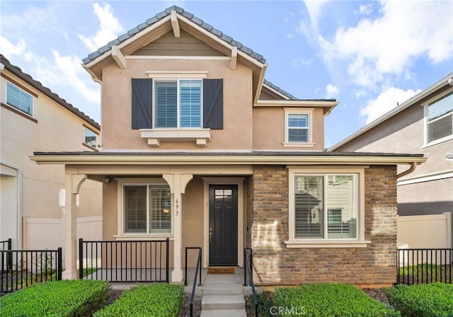 traditional-style home with a porch, fence, stone siding, and stucco siding