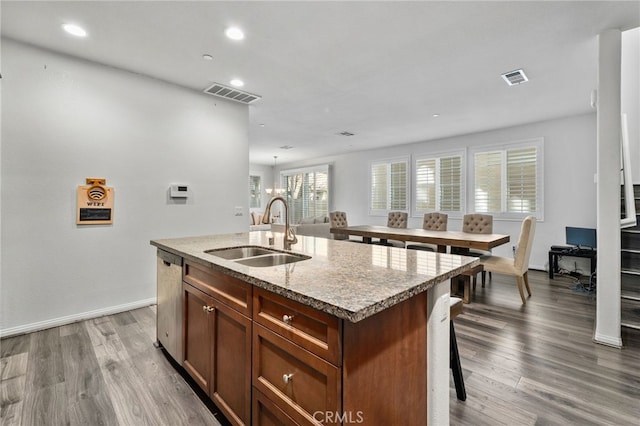 kitchen featuring an island with sink, wood finished floors, visible vents, and a sink