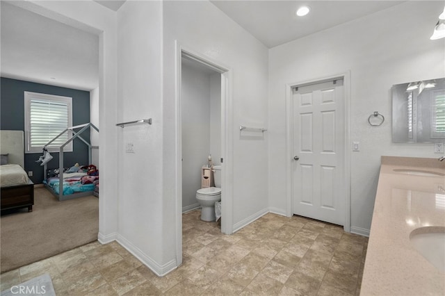 ensuite bathroom with a sink, baseboards, toilet, and double vanity