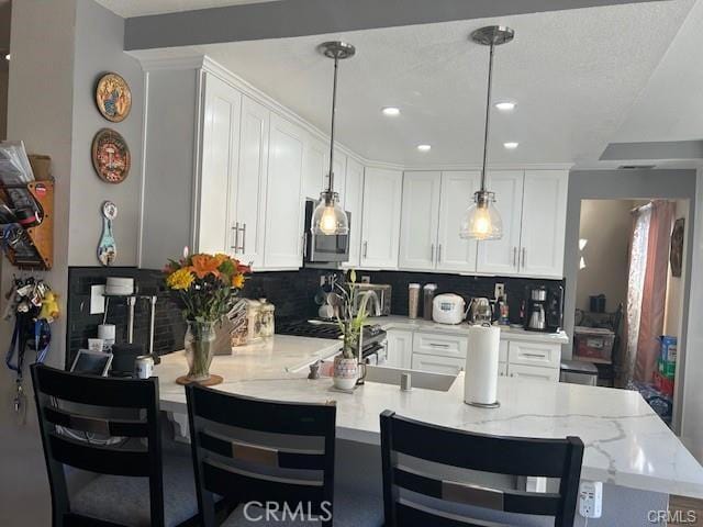 kitchen featuring tasteful backsplash, hanging light fixtures, white cabinets, and a peninsula