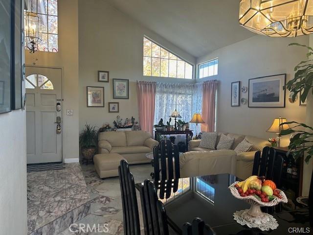 living area featuring baseboards, a notable chandelier, marble finish floor, and high vaulted ceiling