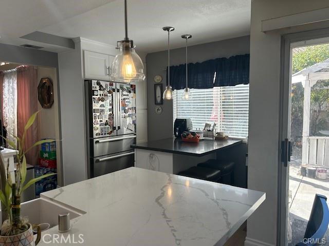 30103 Desert Rose Dr, Castaic, CA 91384 - kitchen featuring freestanding refrigerator, white cabinets, hanging light fixtures, and dark stone countertops