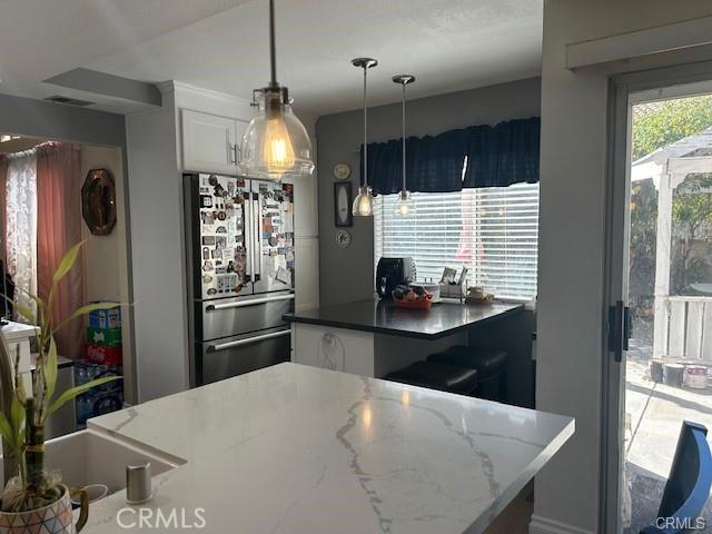 30103 Desert Rose Dr, Castaic, CA 91384 - kitchen with freestanding refrigerator, white cabinetry, decorative light fixtures, and dark stone countertops