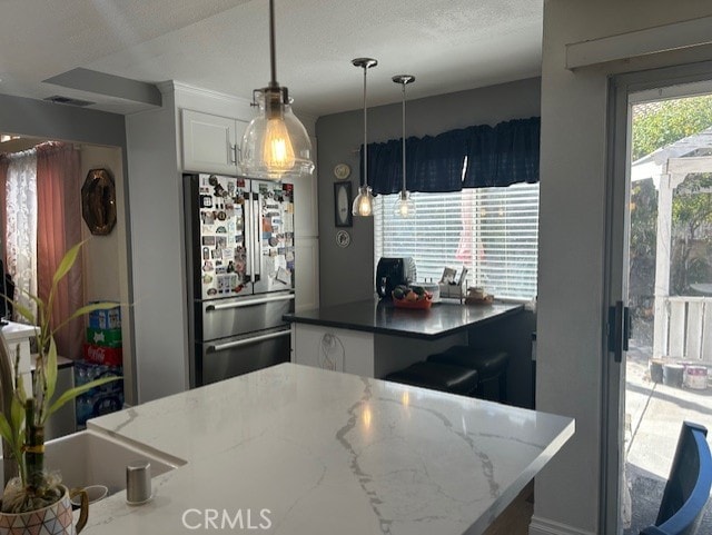 30103 Desert Rose Dr, Castaic, CA 91384 - kitchen with freestanding refrigerator, white cabinets, hanging light fixtures, and dark stone counters