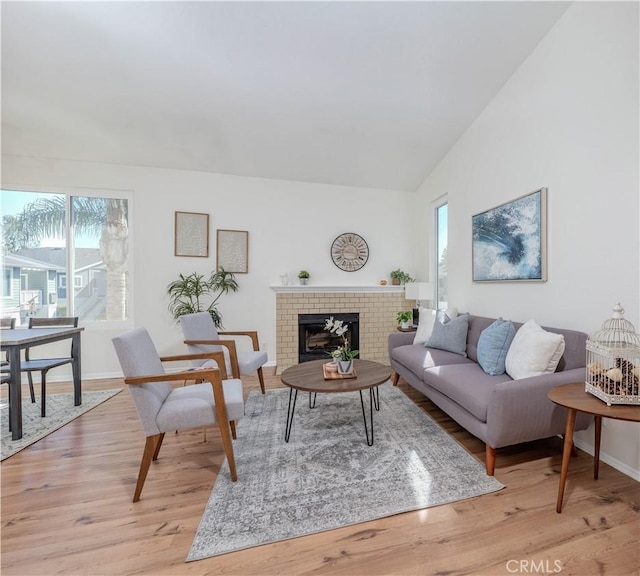 living room featuring a wealth of natural light, light wood-type flooring, a brick fireplace, and vaulted ceiling