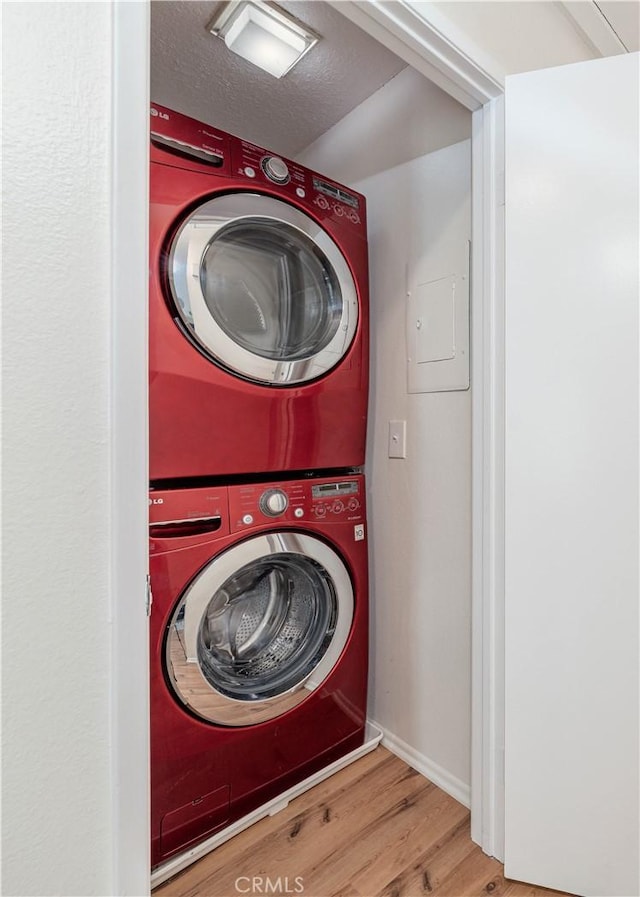 laundry room featuring stacked washer and dryer, electric panel, a textured ceiling, wood finished floors, and laundry area