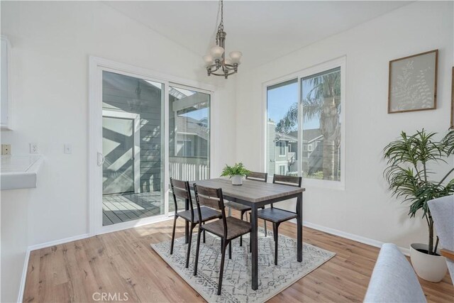 dining room with light wood-type flooring, baseboards, and an inviting chandelier