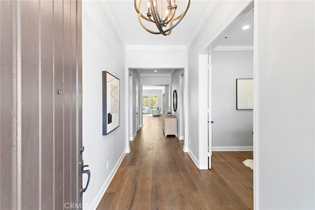 hallway with a chandelier, dark wood-style flooring, baseboards, and ornamental molding