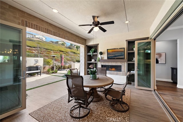 view of patio / terrace with ceiling fan, outdoor dining area, fence, and a lit fireplace