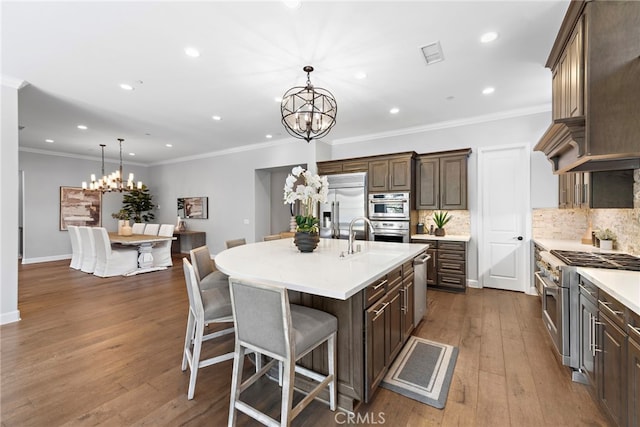 kitchen with dark wood finished floors, an inviting chandelier, a kitchen island with sink, premium appliances, and backsplash