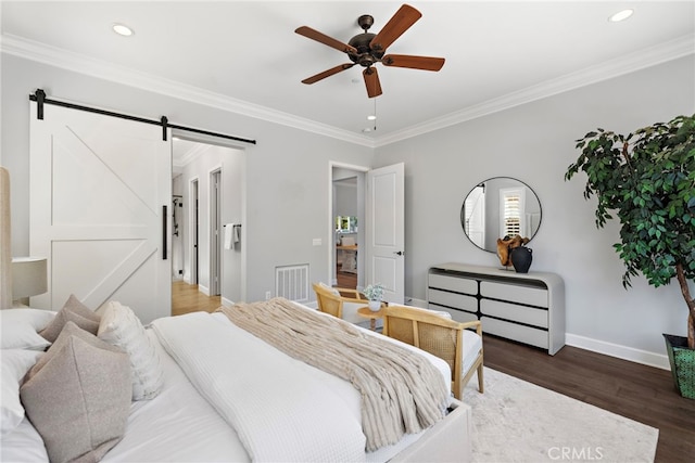 bedroom with baseboards, crown molding, a barn door, and wood finished floors