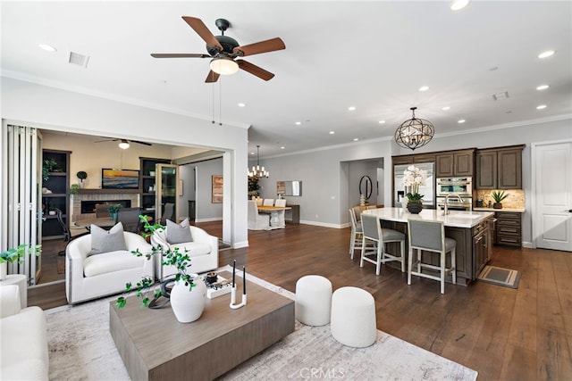 living area with recessed lighting, a brick fireplace, dark wood finished floors, and ceiling fan with notable chandelier