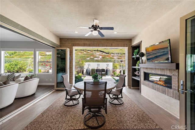 dining room with ceiling fan, recessed lighting, wood finished floors, a glass covered fireplace, and a textured ceiling