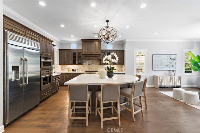 kitchen featuring dark brown cabinetry, decorative backsplash, dark wood finished floors, and stainless steel built in fridge