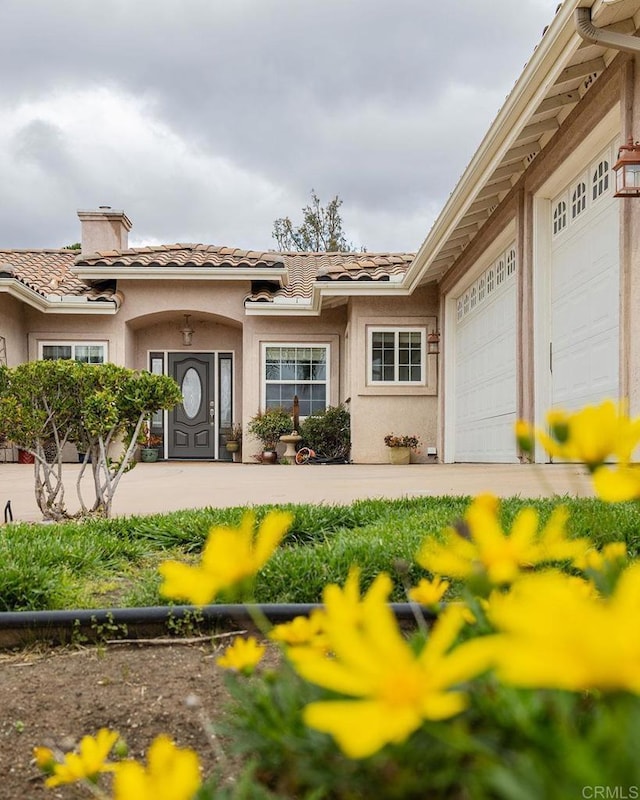 property entrance featuring a tiled roof, a garage, a chimney, and stucco siding