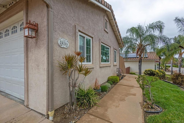 view of side of property with stucco siding, a tile roof, a lawn, and a garage