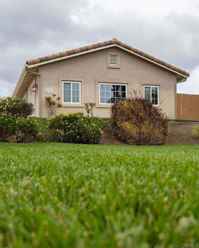 view of side of property with stucco siding, a tile roof, a yard, and fence