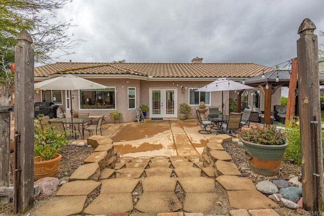 rear view of house featuring a tiled roof, stucco siding, french doors, a chimney, and a patio area