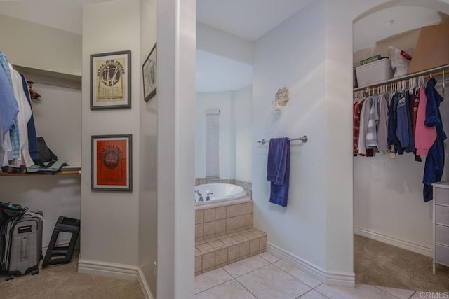 bathroom with baseboards, a garden tub, a spacious closet, and tile patterned flooring