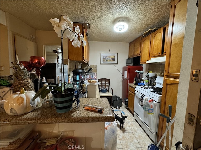 kitchen with brown cabinets, light tile patterned flooring, under cabinet range hood, black microwave, and white gas range