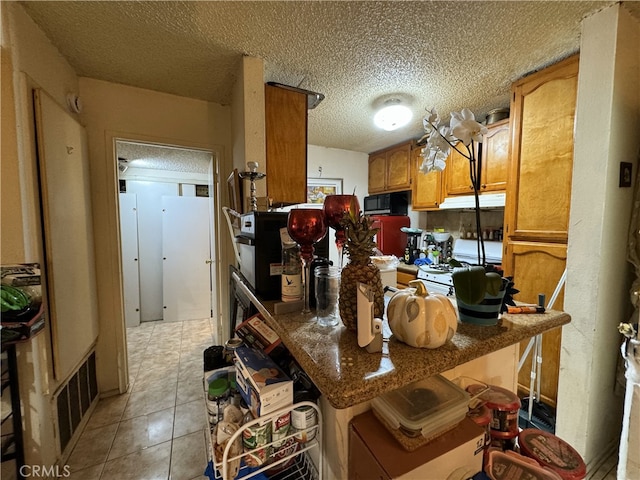 kitchen featuring black microwave, white gas range oven, brown cabinets, light tile patterned flooring, and a textured ceiling