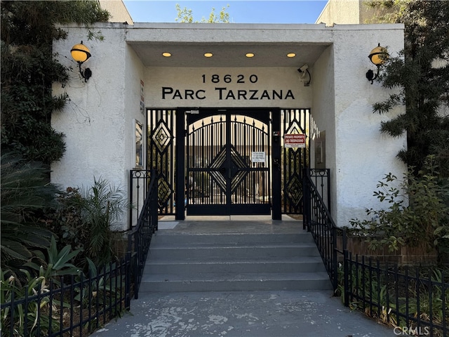 view of exterior entry with stucco siding and fence