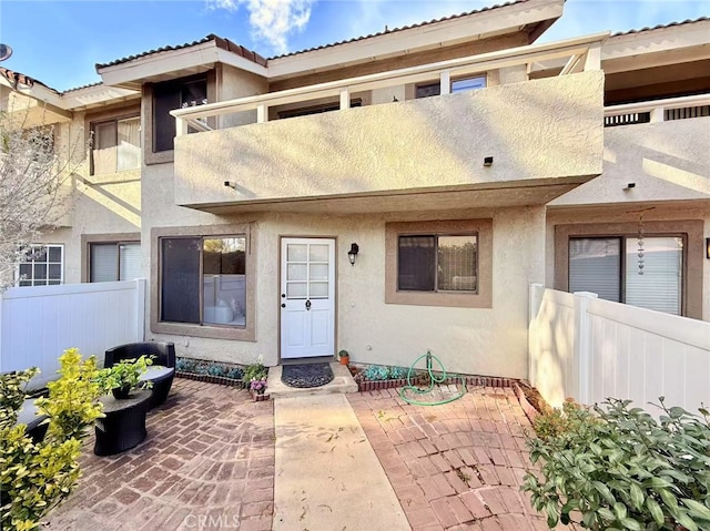 view of front of house with a balcony, stucco siding, a patio, and fence