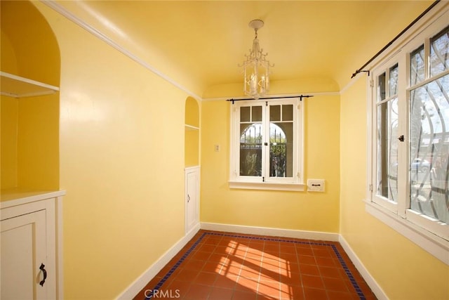 unfurnished dining area featuring baseboards, an inviting chandelier, dark tile patterned flooring, arched walkways, and crown molding