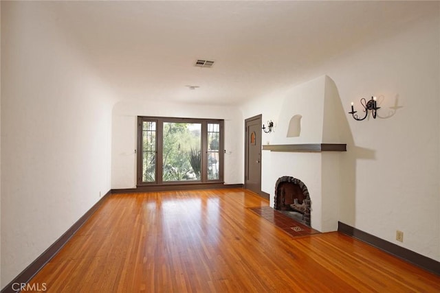 unfurnished living room featuring visible vents, a fireplace with flush hearth, baseboards, and wood finished floors