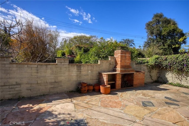 view of patio / terrace with a fenced backyard and an outdoor brick fireplace