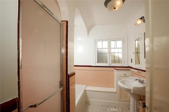 full bathroom featuring a shower with shower door, a wainscoted wall, tile patterned flooring, tile walls, and a bath