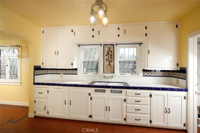 kitchen featuring backsplash, baseboards, tile countertops, white cabinets, and a sink