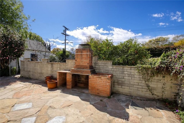 view of patio / terrace featuring an outdoor brick fireplace and fence