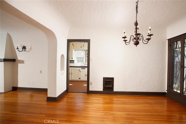 unfurnished room featuring light wood-type flooring, heating unit, arched walkways, baseboards, and a chandelier