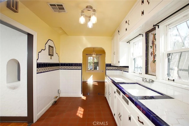 kitchen featuring visible vents, arched walkways, white cabinets, and tile counters