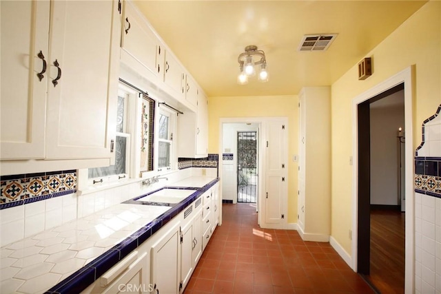 kitchen with visible vents, dark tile patterned floors, a sink, white cabinetry, and tile counters