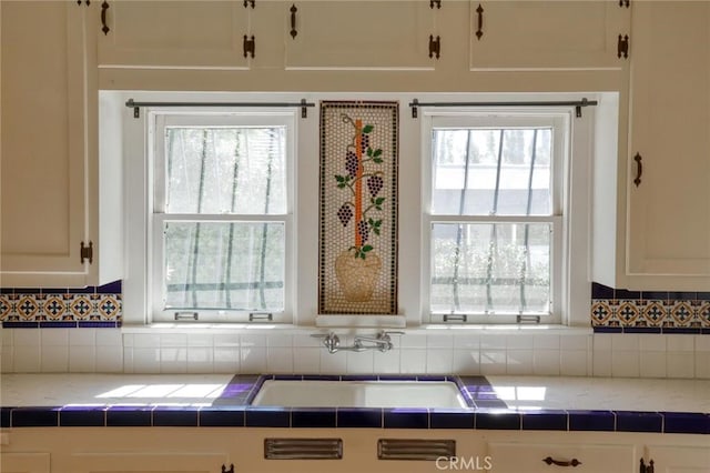 details with tasteful backsplash, white cabinets, tile counters, and a sink