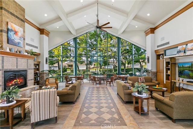 living area with visible vents, a tiled fireplace, beamed ceiling, a towering ceiling, and a ceiling fan