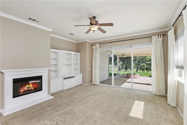 unfurnished living room with a glass covered fireplace, crown molding, visible vents, and carpet floors