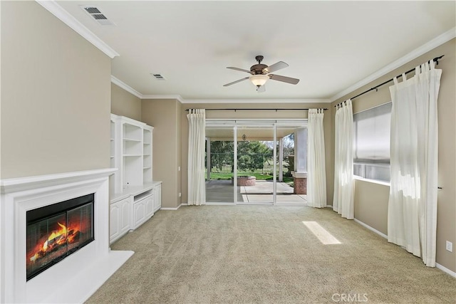 unfurnished living room featuring a glass covered fireplace, light colored carpet, crown molding, and visible vents