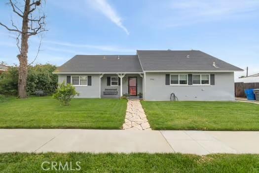 ranch-style home featuring a front lawn, fence, covered porch, and stucco siding