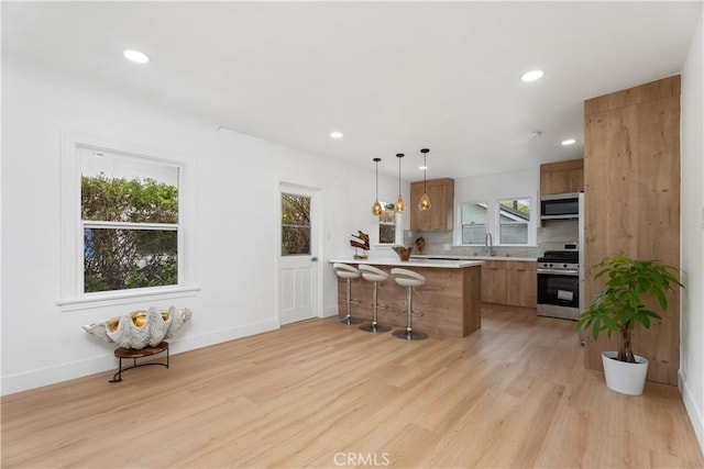 kitchen with stainless steel appliances, a peninsula, brown cabinetry, and light countertops