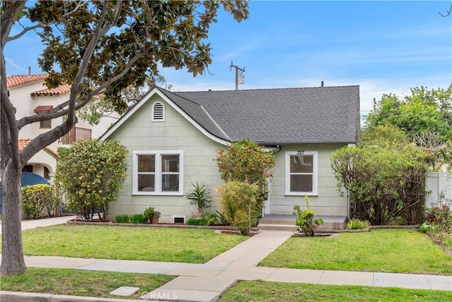 view of front of property with a shingled roof, a front lawn, and fence