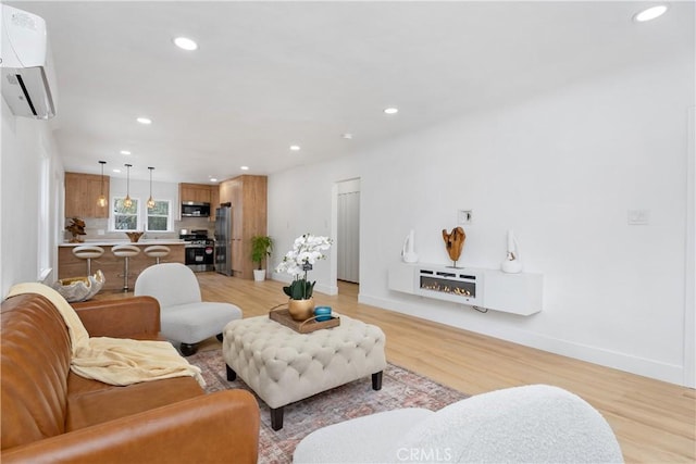 living area with recessed lighting, baseboards, light wood finished floors, and a wall unit AC