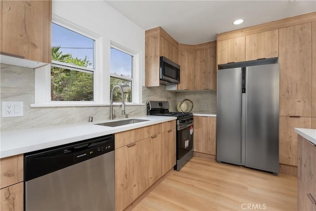 kitchen featuring a sink, tasteful backsplash, light wood-style floors, appliances with stainless steel finishes, and light countertops