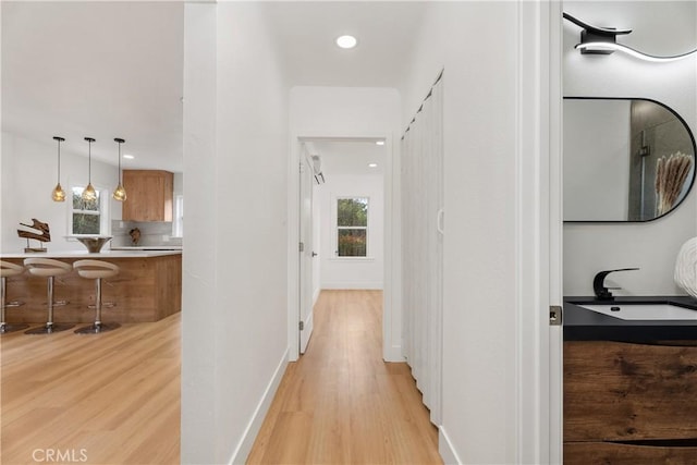 hallway featuring plenty of natural light, baseboards, light wood-type flooring, and a sink